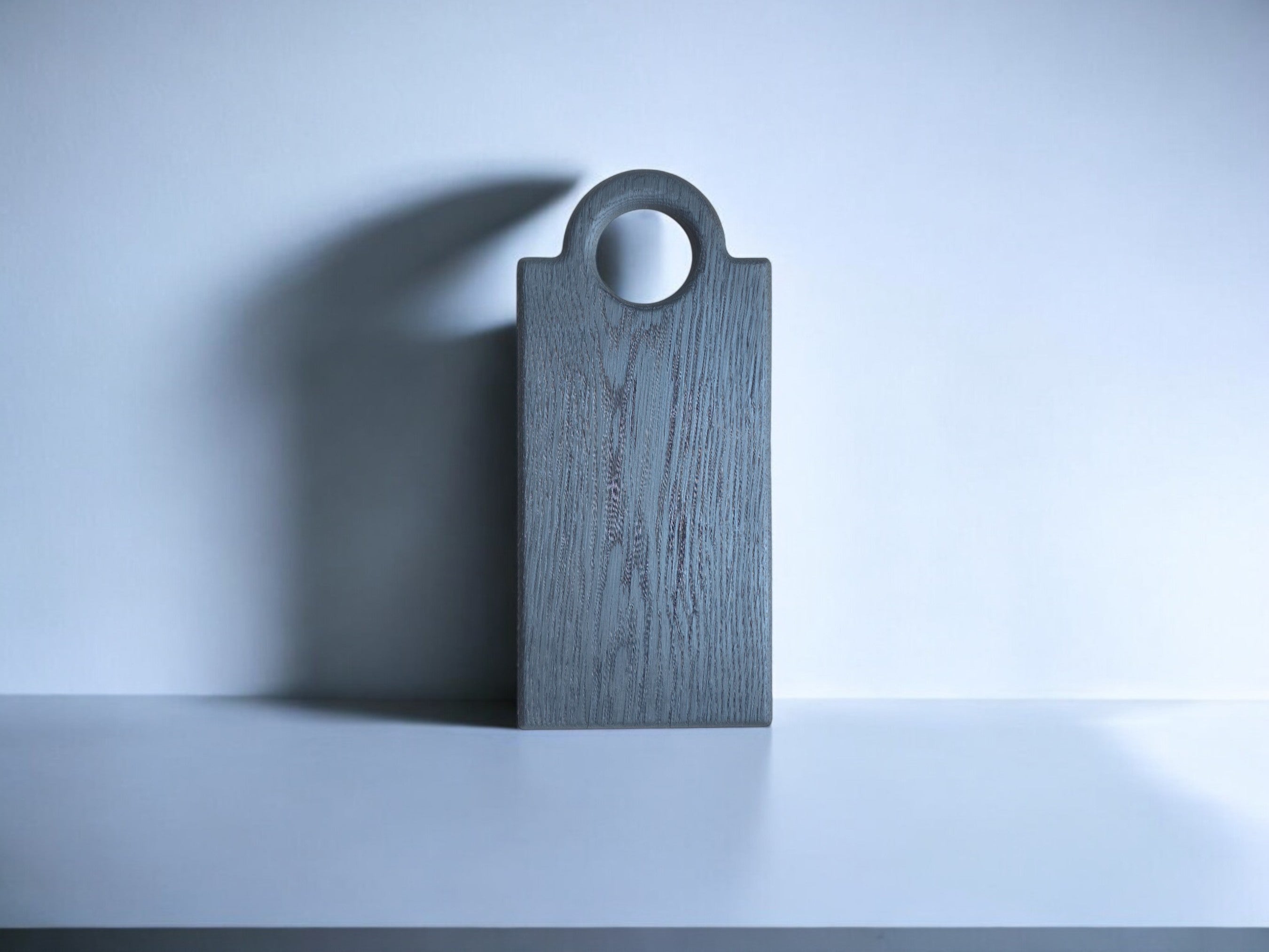 Das Oldrye Schneidebrett "Black Wide Loop" in minimalistischer und stilvoller Präsentation. Das schwarze Brett sticht auf dem weißen Hintergrund hervor, der Schattenwurf betont die Form.