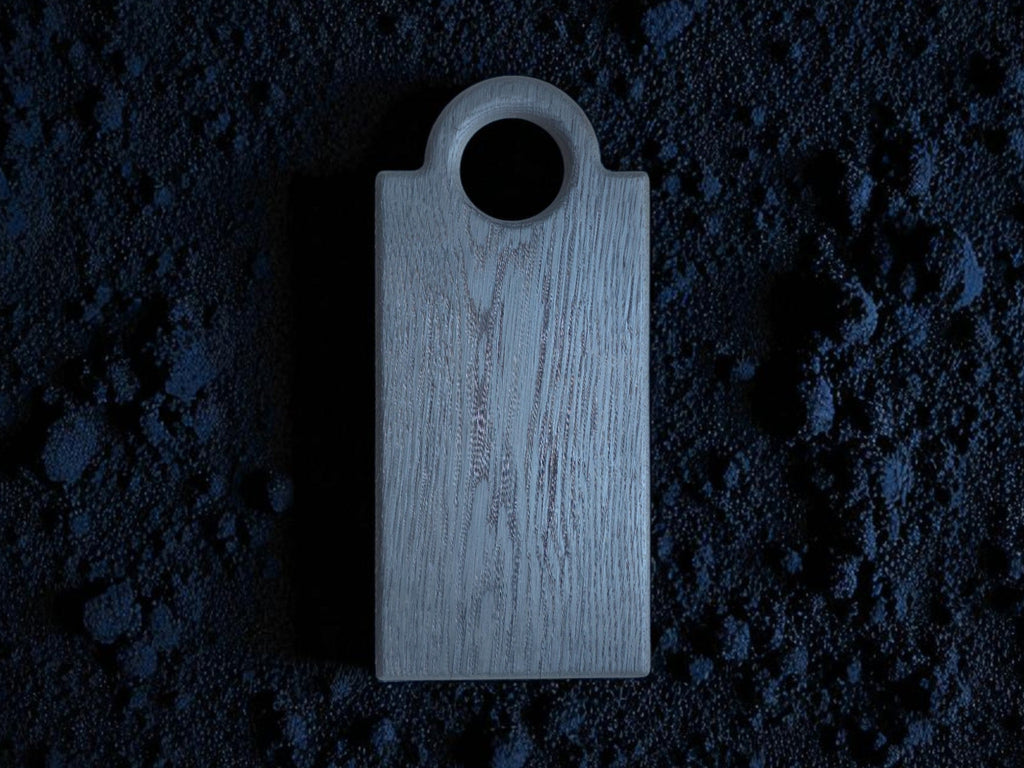 Das Schneidebrett "Oldrye Black Wide Loop" liegt auf einem Bett aus dunklem, blaugrauem Pulver, das die Oberfläche umschließt.