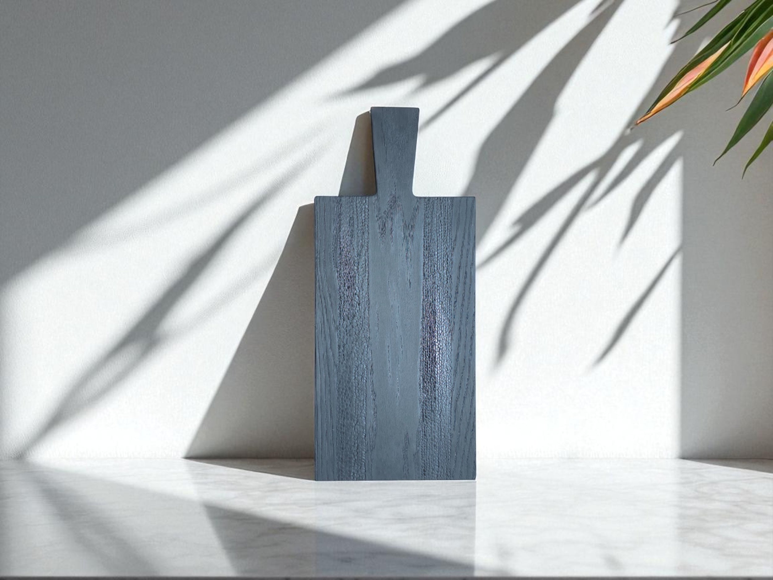 Entdecken Sie die ruhige Eleganz und die einzigartige Textur unseres Black Snake Boards. Dieses handgefertigte Brett aus massiver Eiche wird durch die traditionelle Yakisugi-Methode und unser BURN Painting veredelt. Das Spiel der Schatten an der Wand betont die natürliche Schönheit und die einzigartige Maserung des Holzes. Ein vielseitiges Stück für Ihre Küche und Ihr Zuhause.